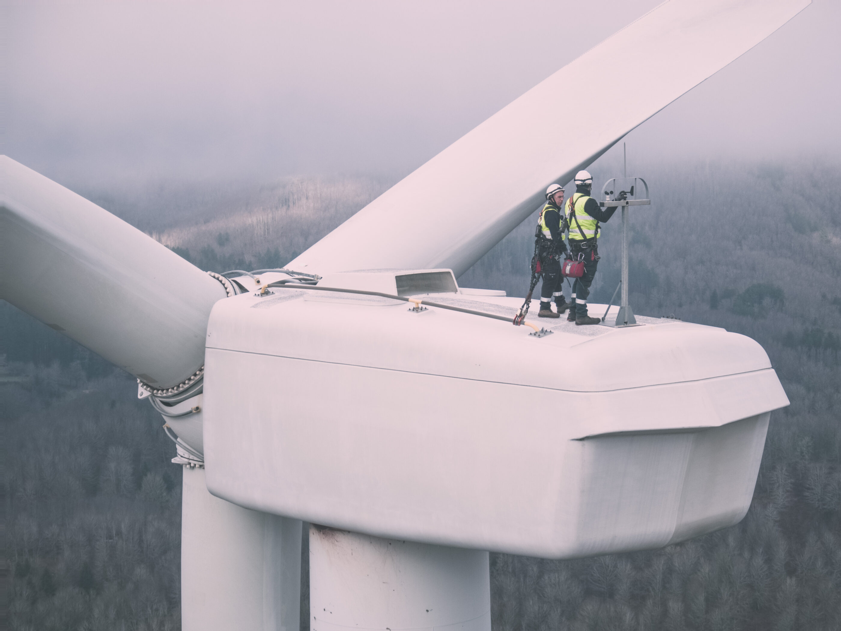 Photo of the top of a wind turbine which is being worked on by two people.
